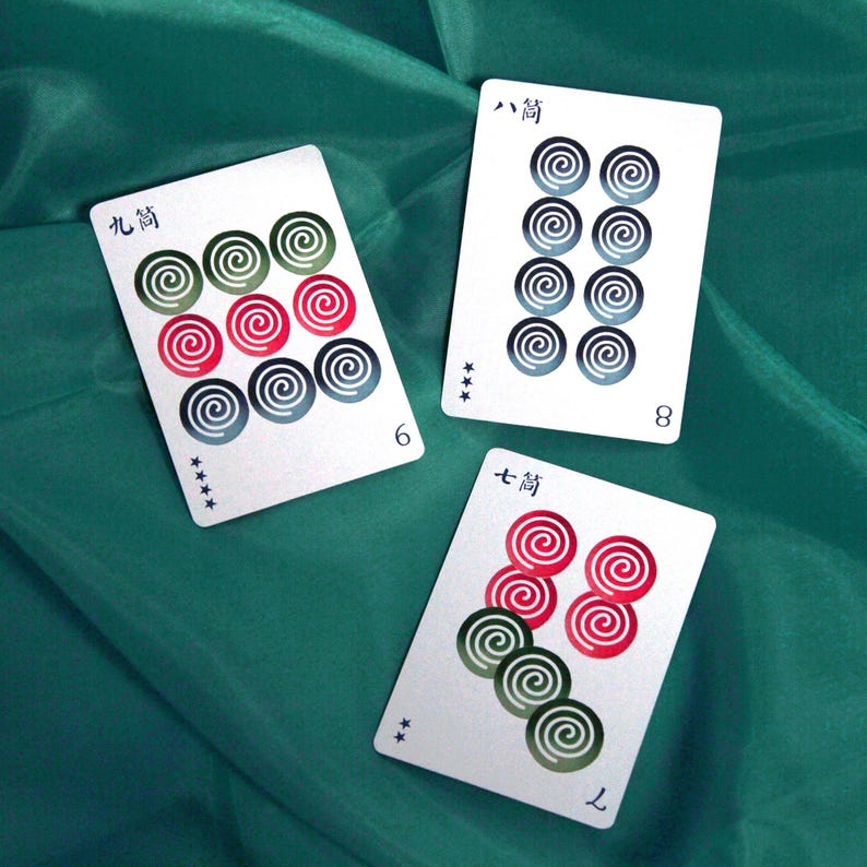 Pu&ograve; includere: Tre carte da gioco bianche con disegni a spirale rossi, verdi e blu sono esposte su un tessuto verde. Le carte sono contrassegnate con i numeri 6, 8 e 7 e caratteri giapponesi. Le carte fanno parte di un gioco di carte.