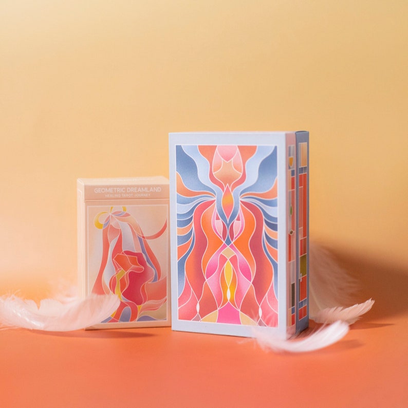 K&ouml;nnte beinhalten: Zwei Schachteln mit Geometric Dreamland Oracle Tarot Journey Karten. Die Schachtel links zeigt eine rosa und orangefarbene Illustration einer Frau mit wallendem Haar. Die Schachtel rechts zeigt ein blaues, rosa und orangefarbenes geometrisches Design.