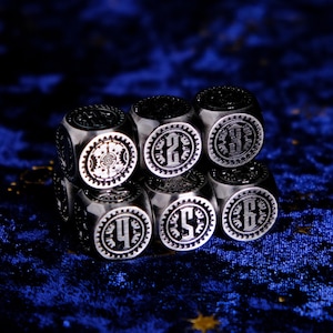 May include: A set of six silver metal dice with black numbers and intricate designs. The dice are arranged in a pyramid shape on a blue velvet surface.