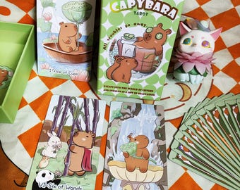 Könnte beinhalten: Ein Capybara-Tarotkartenspiel mit einer grünen Schachtel und mehreren Karten mit Capybara-Illustrationen. Auf der Schachtel steht "CAPYBARA TAROT" und "All troubles go away." Die Karten zeigen verschiedene Szenen mit Capybaras.
