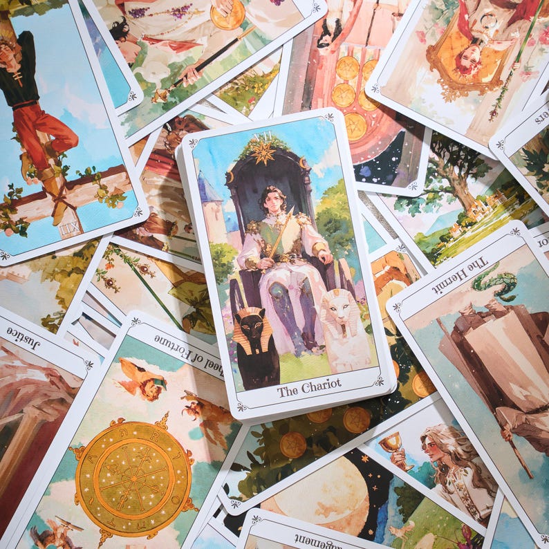 May include: A deck of tarot cards with a central card featuring a person seated on a throne, flanked by a black cat and a white lion. The card is labeled "The Chariot." Other cards are scattered around, depicting various illustrations.