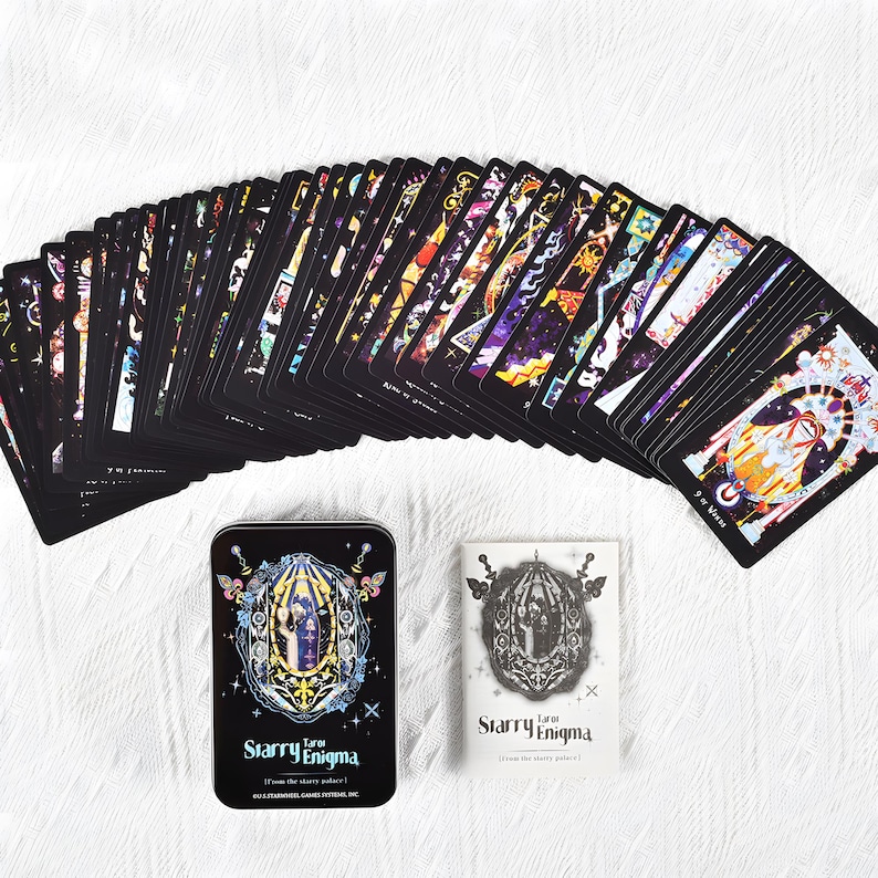 May include: A deck of tarot cards with black card backs and colorful illustrations. The set includes a metal tin and a small booklet, both featuring the text "Starry Enigma". The cards are arranged in a fan shape on a white surface.
