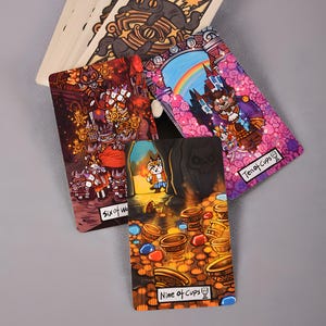 May include: A collection of tarot cards featuring colorful illustrations. The cards display fantasy-themed artwork with characters and symbols. The "Nine of Cups" card shows a character in a cave with treasure. The "Ten of Cups" card shows a character in front of a castle.