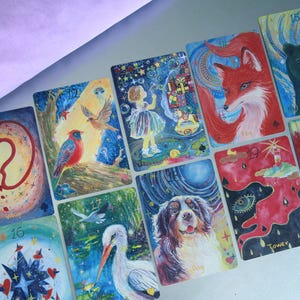 May include: A collection of rectangular oracle cards featuring colourful, detailed illustrations of animals, nature, and symbolic objects. Each card displays a unique painting, including a bear, fox, dog, stork, bird, fountain, and tower, with numbers and text labels.
