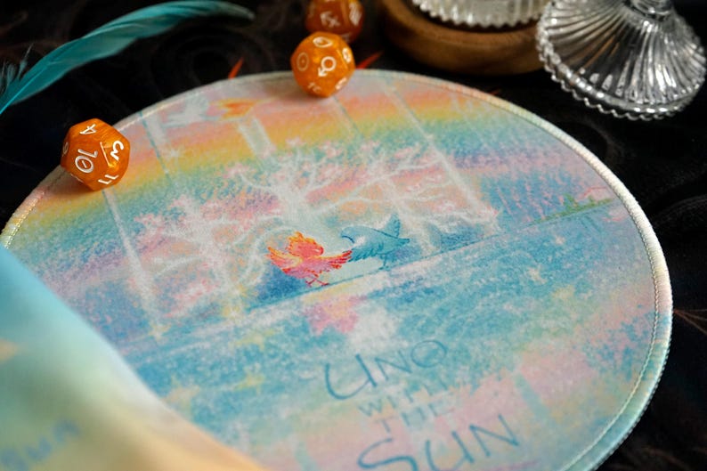 May include: Round, colorful mousepad with a watercolor design featuring two birds and the text "UNO WITH THE SUN." The background has a rainbow gradient. Two orange dice are visible.