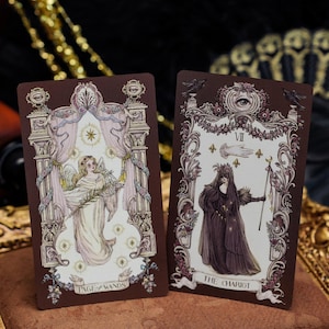 May include: Two rectangular tarot cards with dark brown borders. The left card, labeled Page of Wands, depicts an angel figure in a white robe. The right card, labeled The Chariot, shows a cloaked figure holding a staff beneath an eye symbol.