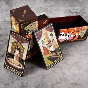 May include: A tarot card deck with a dark brown box featuring the text "FANTASY THE TAROT". Two tarot cards are displayed, one labeled "FIVE OF PENTACLES" and the other "THREE OF PENTACLES". The box and cards have illustrations with a vintage aesthetic.