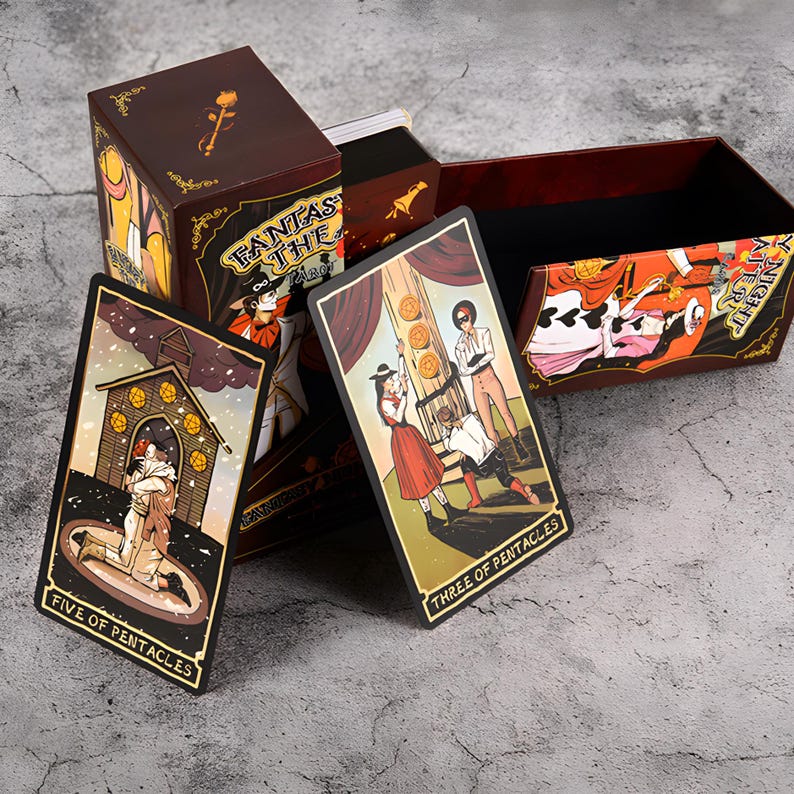 May include: A tarot card deck with a dark brown box featuring the text "FANTASY THE TAROT". Two tarot cards are displayed, one labeled "FIVE OF PENTACLES" and the other "THREE OF PENTACLES". The box and cards have illustrations with a vintage aesthetic.