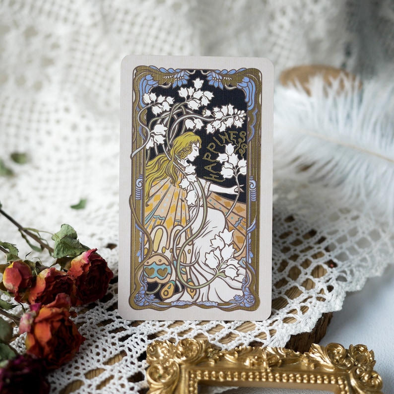 May include: A vintage-style tarot card with a gold frame and a woman in a white dress surrounded by flowers. The card features the word "Happiness" in gold lettering.