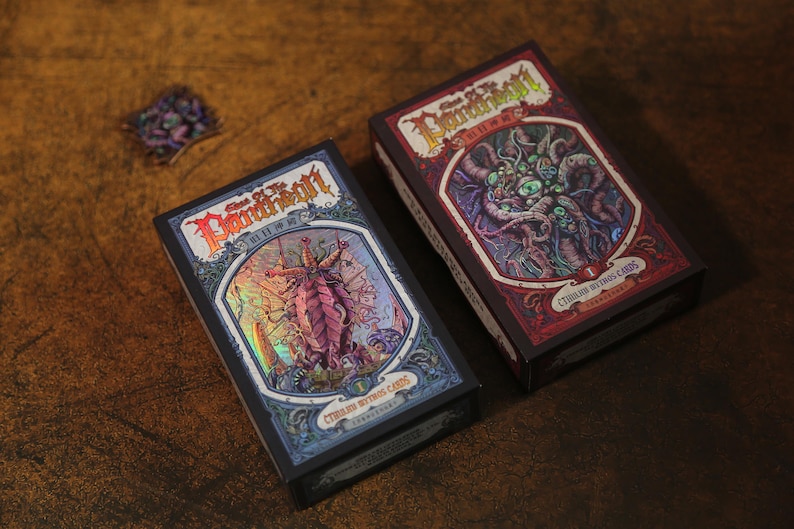 May include: Two rectangular card game boxes titled Call of the Pantheon Cthulhu Mythos Cards. The left box features a holographic blue and purple monster illustration, while the right box displays a red and purple monster with multiple eyes.