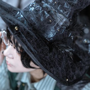 以下が含まれることがあります： 黒い魔女の帽子。尖ったクラウン、レース、羽、小さな金色のスタッドで装飾されています。帽子には装飾的な革バンドがあり、コスチュームやコスプレに適しています。