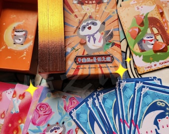 Könnte beinhalten: Ein Tarotkartendeck mit Waschbären-Illustrationen, inklusive einer Schachtel mit der Aufschrift Trash Panda Tarot Card und The Fantastic Journey of Instant Noodles. Die Karten zeigen bunte Zeichnungen von Waschbären, Rosen und Monden mit goldenen Rändern.