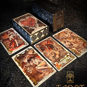 May include: A tarot card deck with decorative metal boxes and several cards displayed. The cards feature detailed illustrations in shades of red, gold, and brown. The text "THREE OF SWORDS", "STRENGTH", and "THE HANGED MAN" are visible.