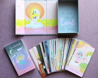 May include: A tarot card deck with a guidebook and box. The box and guidebook feature illustrations of whimsical characters. The cards are fanned out, displaying colourful artwork. The box reads "Welcome to Mr. Butler's World".