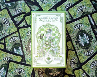 Może przedstawiać: Zielono-białe pudełko talii kart tarota z napisem "Green Trace Tarot" z przodu. Pudełko zawiera zielono-białą ilustrację kobiety trzymającej książkę.