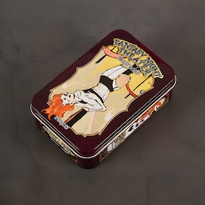 May include: A rectangular, maroon metal tin with a decorative illustration. The illustration features a woman with red hair in a black and white outfit, with the text "FANTASY NIGHT THEATER TAROT CARD" and "POCKET".