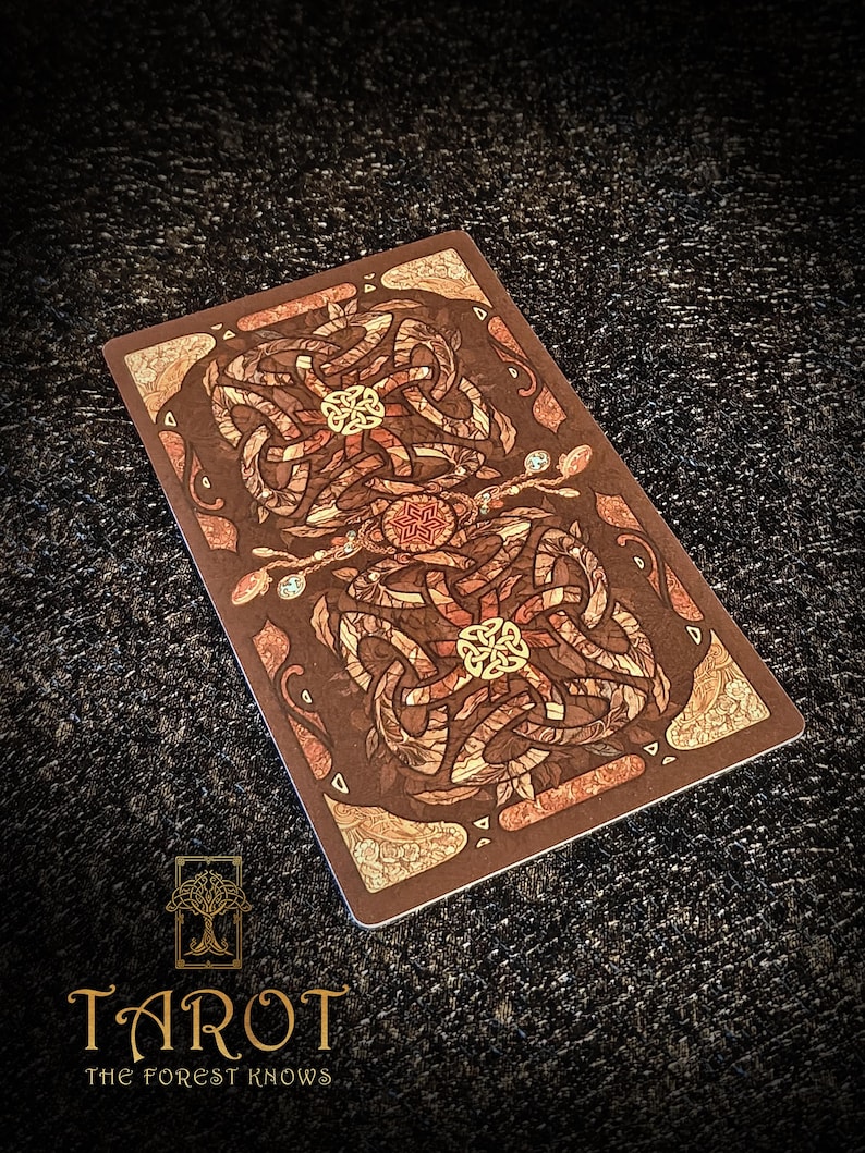 May include: A tarot card with a brown background and detailed Celtic knot patterns in brown, beige, and gold. The card has the text "Tarot The Forest Knows" at the bottom, with a tree logo.