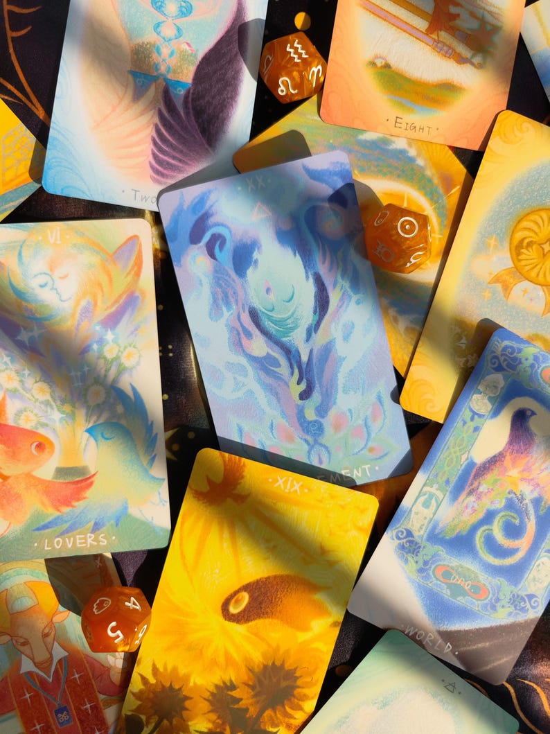 May include: A collection of tarot cards with colorful illustrations and text. The cards feature images of birds, flowers, and abstract designs in shades of blue, yellow, and orange. Several dice are scattered among the cards.