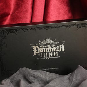May include: A rectangular black box featuring ornate decorative borders and silver text that reads Gaze of the Pantheon, with additional Chinese characters, Limited Edition, and Art Cards of Cthulhu Mythos printed on the front surface.