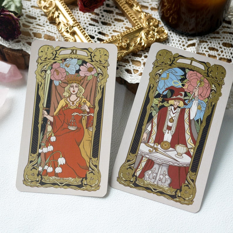 May include: Two tarot cards with gold trim and ornate designs. The card on the left features a woman in a red robe holding a sword and scales. The card on the right features a man in a red robe holding a sword and a cup.