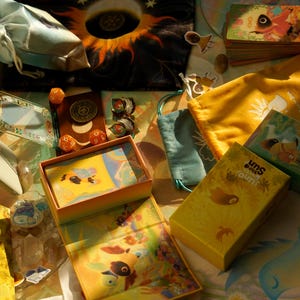 May include: An assortment of colorful board game components, including a yellow box with the text "Uno The Sun", dice, cards, and small drawstring bags. The image features a celestial theme with sun and star motifs.