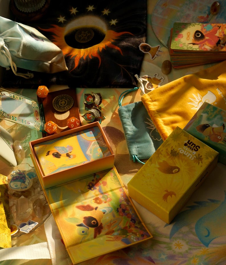 May include: An assortment of colorful board game components, including a yellow box with the text "Uno The Sun", dice, cards, and small drawstring bags. The image features a celestial theme with sun and star motifs.