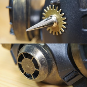 May include: A steampunk-style gas mask with a gold and black finish. The mask has a large, round, gear-shaped detail on the side, a pointed metal spike, and a small, round, metal vent on the front.