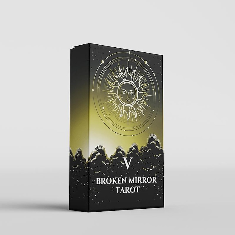May include: A rectangular tarot deck box with a black and gold gradient background. The front features a gold sun illustration with a face, surrounded by celestial rings and stars above black clouds. The text reads V BROKEN MIRROR TAROT.