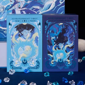 Può includere: Due scatole di carte dei tarocchi con illustrazioni di creature marine e la scritta "SEA IN MOONLIGHT TAROT". Una scatola è azzurra con la scritta "NEW > > > MOON". L'altra scatola è blu scuro con la scritta "...SECLUDED SEA..."