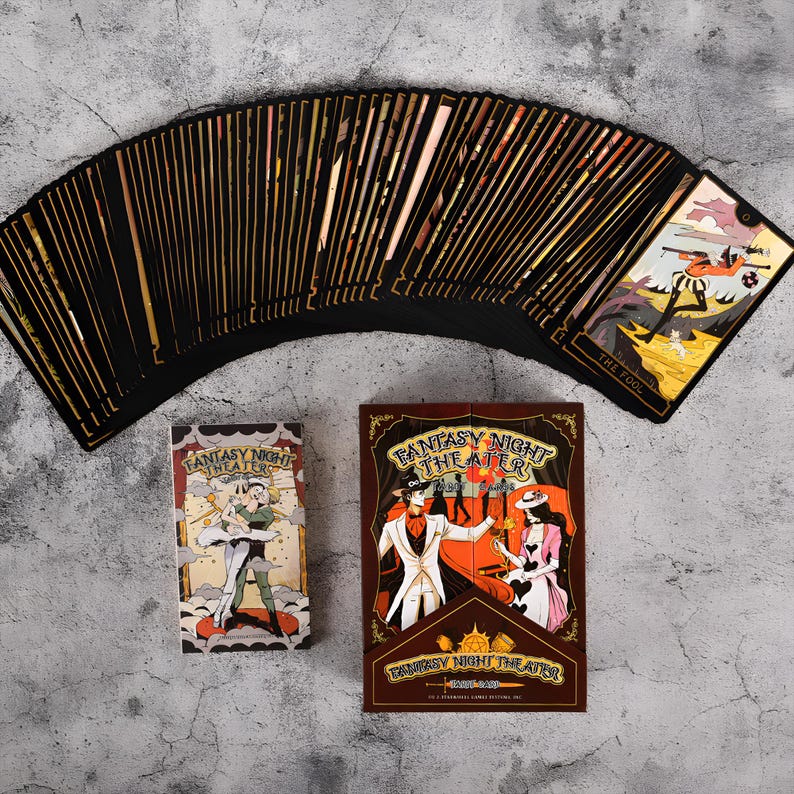 May include: A deck of tarot cards with black card backs and gold edges, fanned out on a gray surface. The box and card backs feature the text "Fantasy Night Theater" and illustrations of figures in vintage attire. One card shows "The Fool".