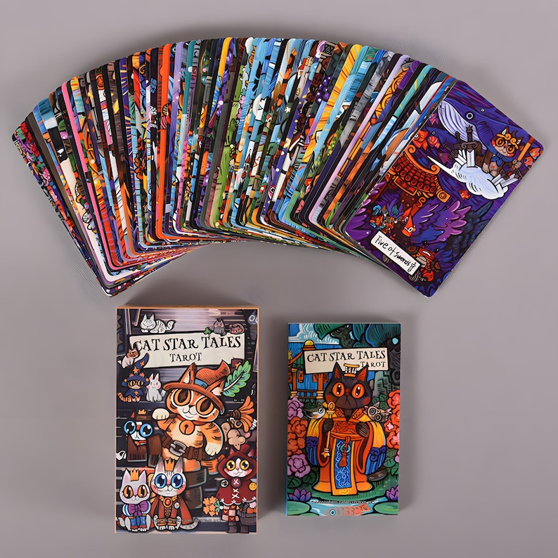May include: A deck of Cat Star Tales Tarot cards fanned out, with two boxes below. The cards feature colorful illustrations of cats in various scenes. The boxes display the title "Cat Star Tales Tarot" with cat-themed artwork.