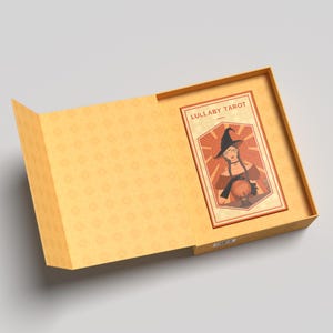 K&ouml;nnte beinhalten: Ge&ouml;ffnete Schachtel mit einer Tarotkarte mit einer Hexenillustration. Die Karte tr&auml;gt die Aufschrift "Lullaby Tarot" und hat eine Vintage-&Auml;sthetik mit Orange-, Braun- und Beiget&ouml;nen. Die Schachtel ist hellorange mit einem geometrischen Muster.