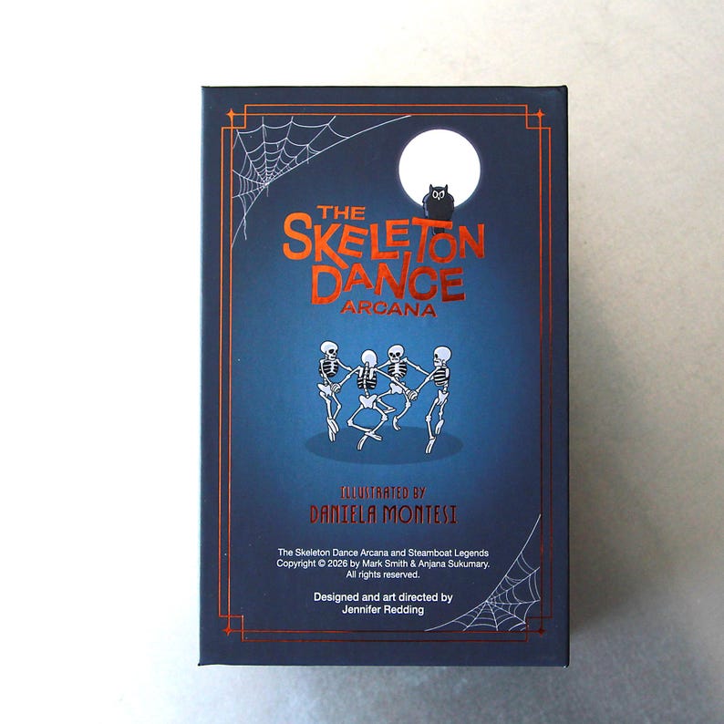 May include: A dark blue box featuring the text "The Skeleton Dance Arcana" in orange. The image includes illustrations of dancing skeletons, a full moon, a black owl, and spiderwebs. The box is designed by Jennifer Redding and illustrated by Daniela Montesi.