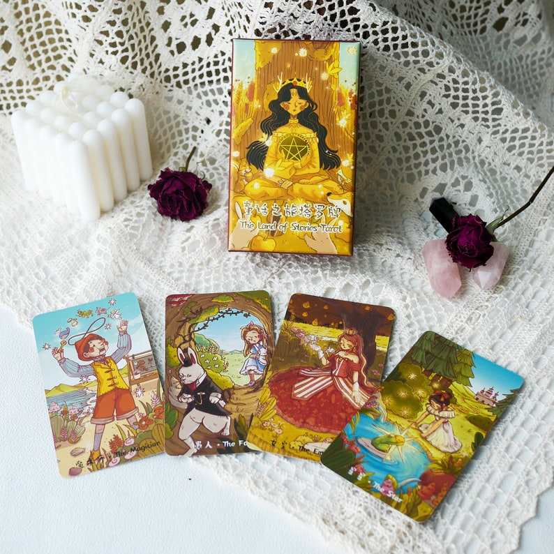 May include: A set of five tarot cards with colorful illustrations. The cards feature a variety of characters, including a magician, a fox, a princess, and a fairy. The cards are from the "The Land of Stories Tarot" deck.