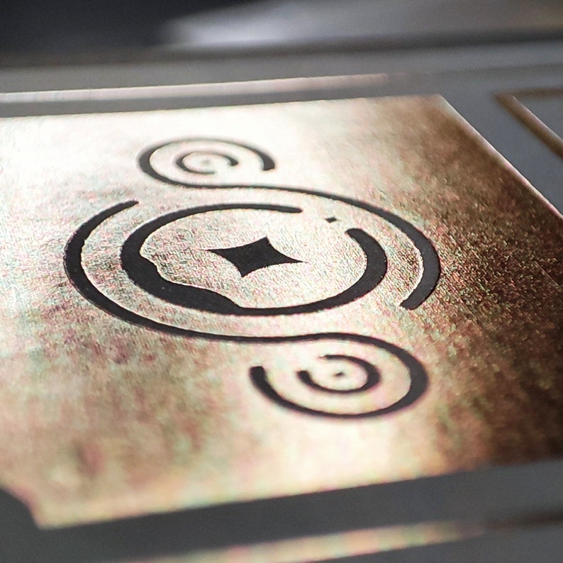 May include: A gold metallic background with a black design of a circle with a diamond in the center and two smaller circles around it.
