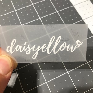Puede incluir: Una lámina de vinilo transparente con la palabra "daisyellow" escrita en letras cursivas blancas.