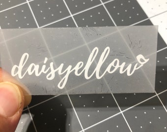 May include: A clear vinyl sheet with the word "daisyellow" written in white cursive lettering.
