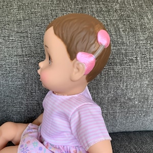 May include: A pink and white striped dress with a floral print skirt on a doll with brown hair and pink ear pieces.