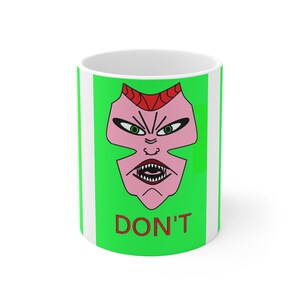May include: White ceramic mug with a green background and a pink devil face design. The devil face has red horns, green eyes, and sharp teeth. The word "DON'T" is printed in red below the face.
