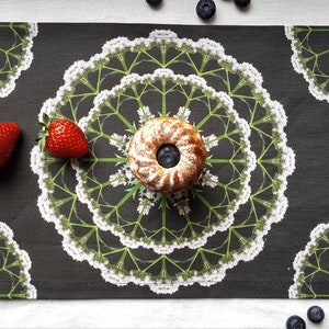 May include: A black and white floral patterned placemat with a small cake and strawberries on top. The cake is topped with a blueberry.