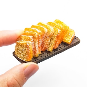 Op de afbeelding: Een miniatuur houten dienblad met een stapel oranje en gele miniatuur broodplakjes.