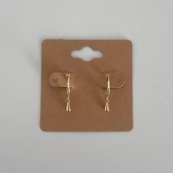 Könnte beinhalten: Ein Paar goldene Creolen mit einem kleinen tropfenförmigen Anhänger an jedem Ohrring.
