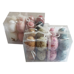May include: Two clear plastic boxes filled with decorative Easter eggs. The eggs are in various shades of pink, blue, brown, and white with speckled patterns. The boxes are tied with white ribbon.