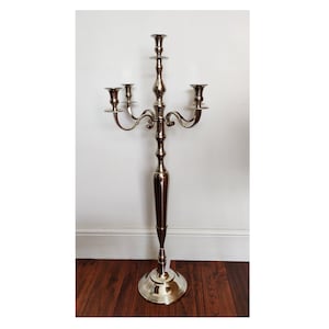 May include: A tall, silver candelabra with five candle holders. The candelabra has a round base and a slender, ornate stem. The candle holders are curved and extend outwards. The candelabra is approximately 152 cm tall.