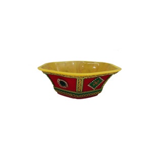 May include: A yellow and red decorative bowl with gold trim and green accents. The bowl is made of plastic and has a unique design.