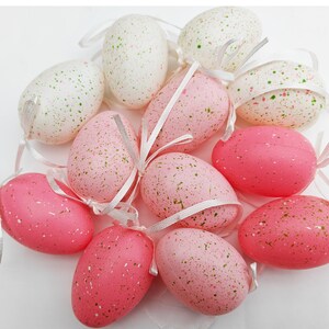May include: A collection of pink and white speckled Easter eggs with white ribbon bows.
