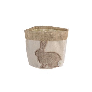 May include: A beige burlap Easter basket with a brown bunny silhouette and a white pom-pom tail.