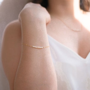 May include: A delicate gold chain bracelet with a row of small white pearls.