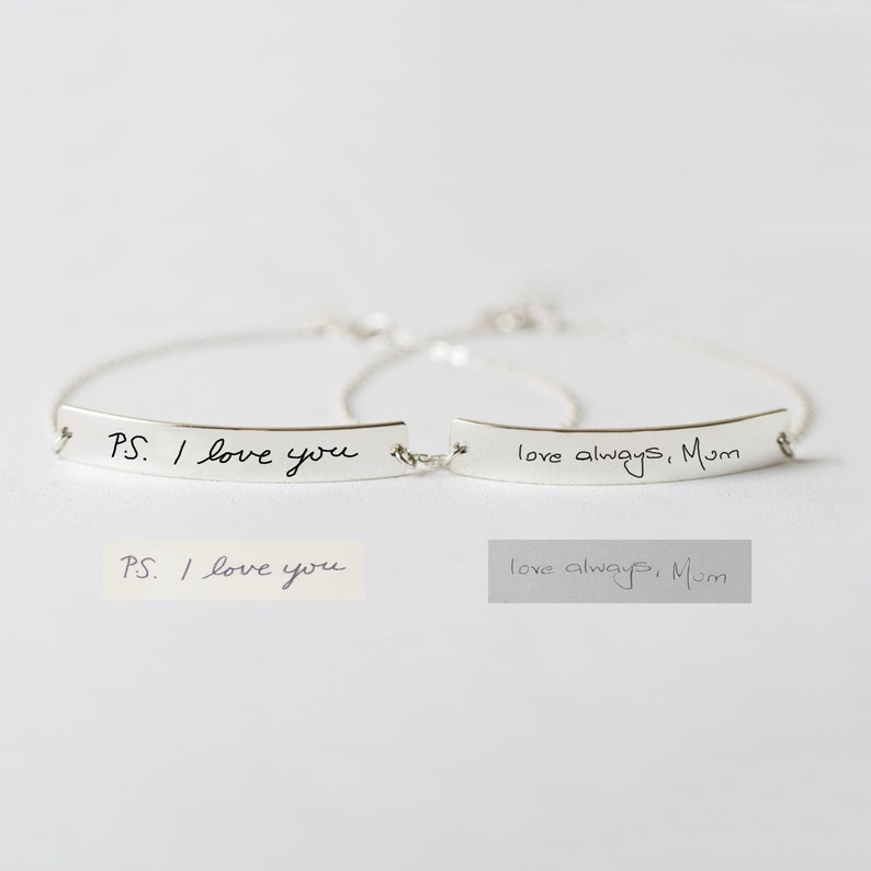 Puede incluir: Dos pulseras de plata con un mensaje escrito a mano en cada una. La primera pulsera dice "P.S. Te quiero" y la segunda pulsera dice "Te quiero siempre, Mam&aacute;".