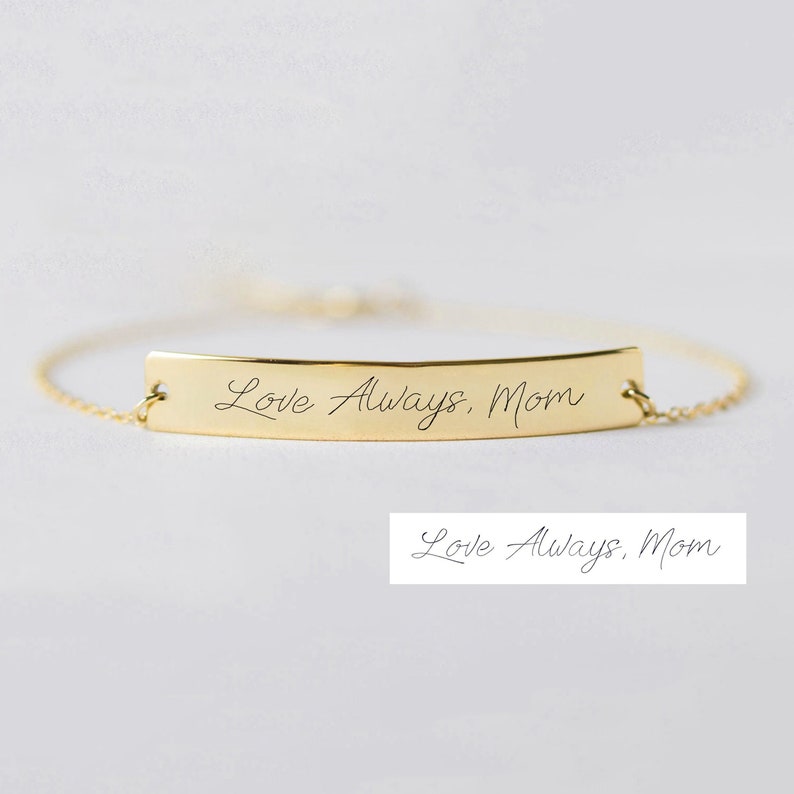 Puede incluir: Pulsera de oro con una cadena delicada y un dije plano en forma de barra grabado con el mensaje escrito a mano "Love Always, Mom".